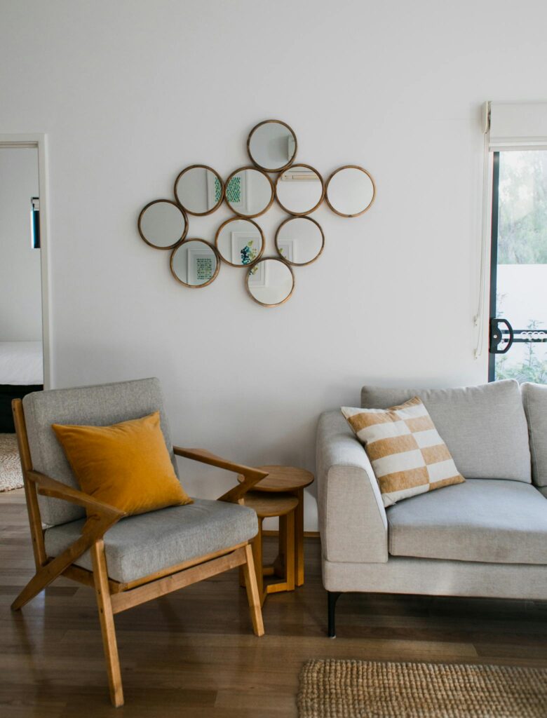 Contemporary living room featuring a gray sofa, wooden armchair, and circular mirrors on a white wall.