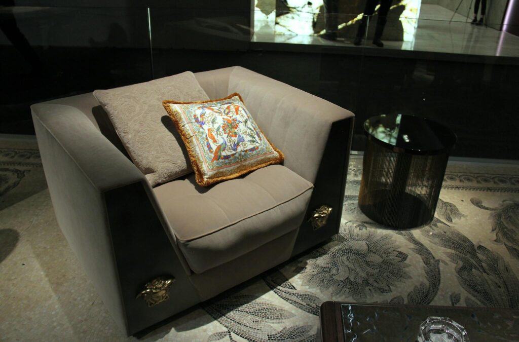 Luxurious armchair with ornate cushion and glass side table in a modern setting.